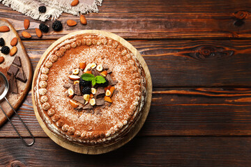 Delicious crepe cake with chocolate, nuts, blackberries and cocoa powder on wooden table, flat lay. Space for text