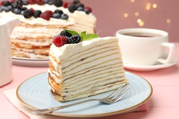 Piece of tasty crepe cake with berries served on pink wooden table against blurred lights, closeup