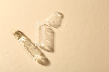 Glass ampoules with cosmetic product and water drops on beige background, flat lay. Space for text