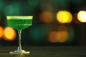 Glass of alcoholic cocktail on table against blurred background. Space for text