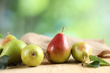 Fresh ripe pears and green leaves on wooden table outdoors, closeup