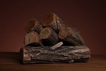 Pile of cut firewood on wooden table against brown background, closeup