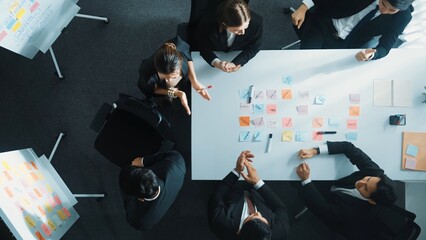 Top view of investor writing white board to present project and putting hand together with professional business team to celebrate successful project at meeting table with sticky note. Directorate.