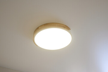 A round ceiling light with a light wood rim shines brightly against a white ceiling