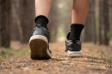 Children feet in black sneakers walking through forest, closeup.