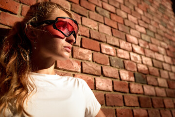 Young woman wearing red sports glasses standing against a brick wall exterior