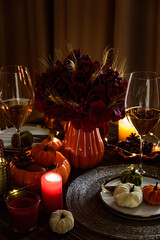 Thanksgiving table setting with decorative pumpkins, candles and string lights on dark wooden table