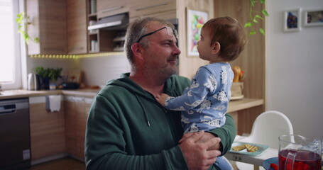 Father holding toddler and smiling, engaging in a playful and affectionate moment during family...
