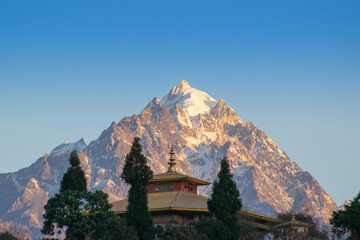 Beautiful light from sunrise on snow peak of Mount Siniolchu, one of the tallest mountains of the Indian state of Sikkim. 6,888 metres (22,598 ft). Ravangala monastery in foreground. Sikkim, India.