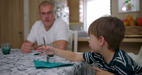 Man and boy sharing a quiet moment at the table, while a woman works in the background, showcasing a candid family interaction in a cozy home setting