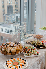 Delicious spread of food on a table with a city view during a gathering in a bright indoor space