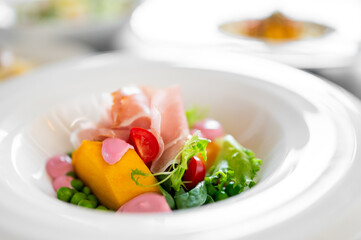 Gourmet salad with prosciutto, cherry tomatoes, peas, squash, greens, and pink sauce, artistically...