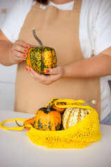 woman in apron puts pumpkins out of woven bag on kitchen table