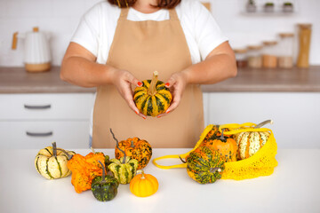 Woman Holding Mini Pumpkins in Woven Bag on Kitchen Table