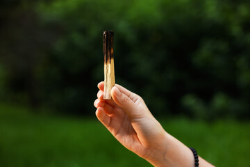 Woman meditating with Palo Santo stick to heal or restore her aura outdoors, closeup