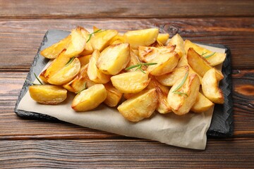 Tasty baked potatoes with rosemary on wooden table, closeup