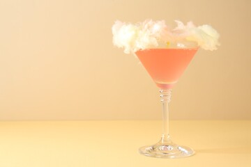 Tasty cocktail decorated with cotton candy on color background, space for text
