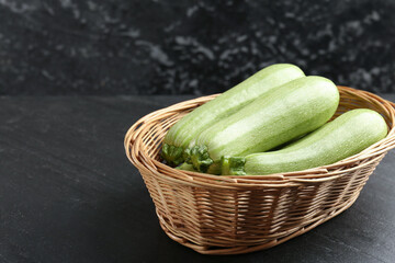 Fresh ripe zucchinis in wicker basket on black textured table, closeup. Space for text