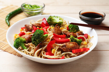 Delicious noodles with meat and vegetables served on light wooden table, closeup