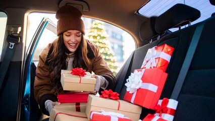 Happy woman delivering Christmas gifts to friends and family, packing Xmas presents to her car,...