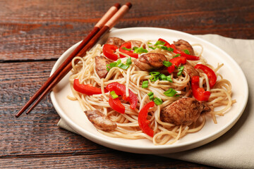 Tasty noodles with chicken, green onions and vegetables served on wooden table, closeup
