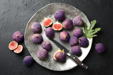 Fresh ripe figs, knife and green leaf on black textured table, flat lay