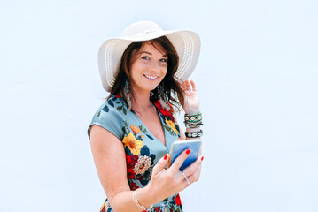 Portrait of smiling woman in blue dress and hat using mobile phone on white background