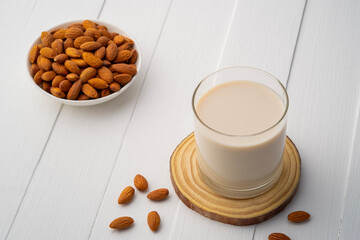 Almond milk in the glass with almond on wooden plate.