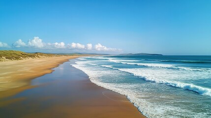 Obraz premium A bright, sunny day on a pristine beach with golden sand in the foreground and powerful turquoise-blue ocean waves crashing onto the shore
