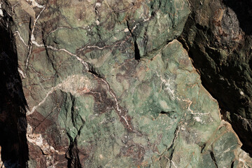 texture di superficie rocciosa ruvida e naturale dalle sfumature di verde, azzurro e grigio, con venature e piccole crepe superficiali