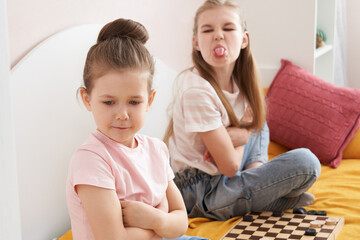 Two sisters playing checkers on a bad and having small fight