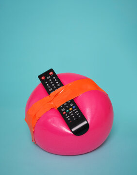 Pink exercise ball with TV remote taped on blue background
