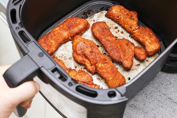 Crispy fried meat fillets cooking in air fryer basket. Golden breaded pieces of meat roasted without oil. Healthy homemade food preparation. Modern electric kitchen appliance for diet cooking.