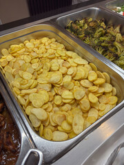 Roasted potato slices in a large buffet tray next to roasted broccoli, food for all-inclusive resort, catering, and restaurant business.