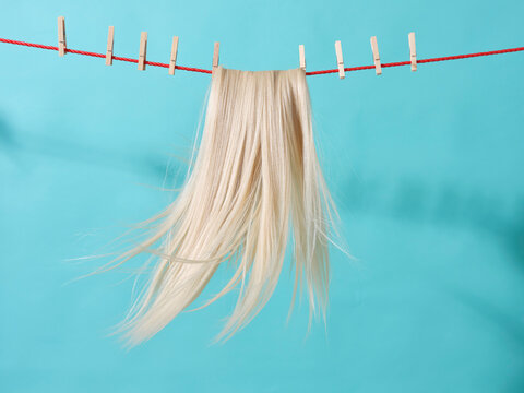 Platinum blonde hair drying on red line with  pegs on blue background