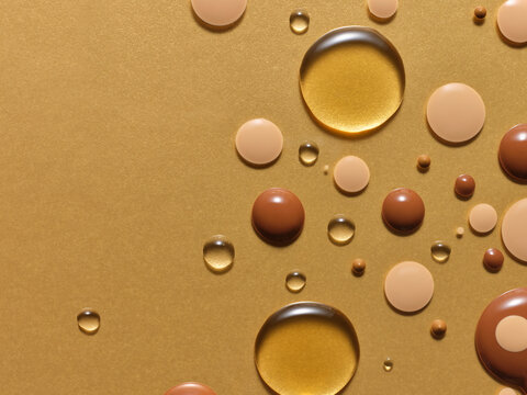 Droplets of oil, serum and tanning lotion on a gold surface