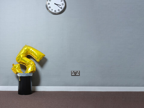 Balloon in the shape of the number 5 in bin next to a wall in office