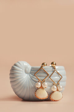 Gold seashell earrings with pearls on ceramic shell stand
