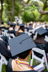 Selective focus photo of student sitting at an outdoor graduation, with focus on mortarboard hat...