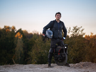 A man poses near an electric monowheel against a forest background. Modern urban transport for active travel. Equipment for safe driving © pavelkant