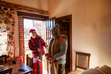 Two friends step inside their cozy rural cabin, warmly dressed and smiling with excitement as they begin their relaxing winter getaway