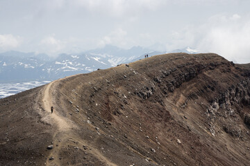 Majestic mountain landscape. Hikers walk along the rim of a volcanic crater. Travel, tourism and hiking on the Kamchatka Peninsula. Nature of the Far East of Russia. Gorely volcano, Kamchatka Krai.