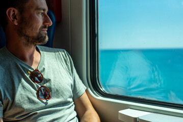 Man Gazes out at Ocean View From Train Window During Daytime