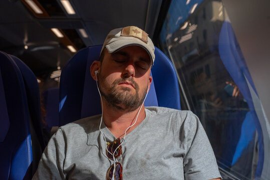 Man Wearing a Cap Listens to Music on a Train During Daylight