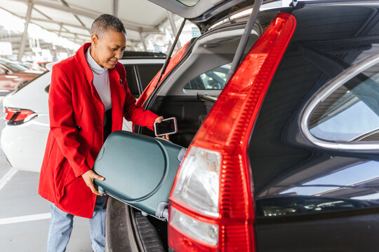 a woman putting her suitcase in the car