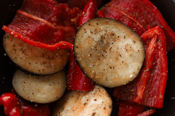 Raw vegetables, chopped peppers and eggplants lie in a bowl, seasoned with spices.