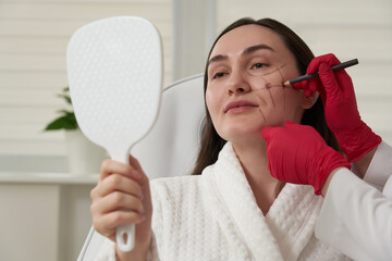 Cosmetologist using facial marker on patient face before beauty treatment in spa salon
