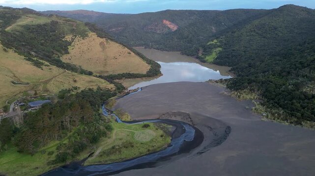 Drone view of Lake Wainamu nestled between forested hills and black sand plains near Bethells Beach