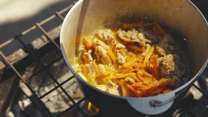 Meat with carrots and ground black pepper is boiled in a pot in nature, the pan is steaming and bubbling with protein broth, tourist recreation, food on the fire, a happy family dinner.