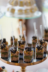 Wedding mini desserts in transparent cups with chocolate, cream and pistachios on golden tray.